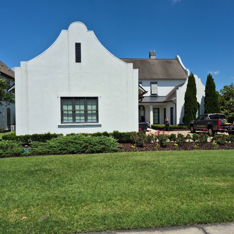 Green front lawn and landscaped beds beside a white stucco home in Livingston Parish